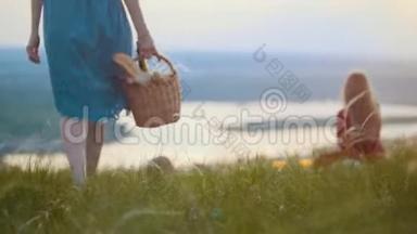 两个可爱的女人坐在田野上野餐-一个女人拿着篮子，拿着面包和葡萄酒，坐着